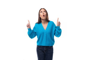 Açık makyajlı, beyaz arka planda mavi düğmeli süveter giyen, esmer, genç ve şaşkın bir kadın..