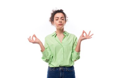 Süslü, genç, kıvırcık saçlı, at kuyruklu, yeşil gömlekli bir kadın meditasyon yapıyor..