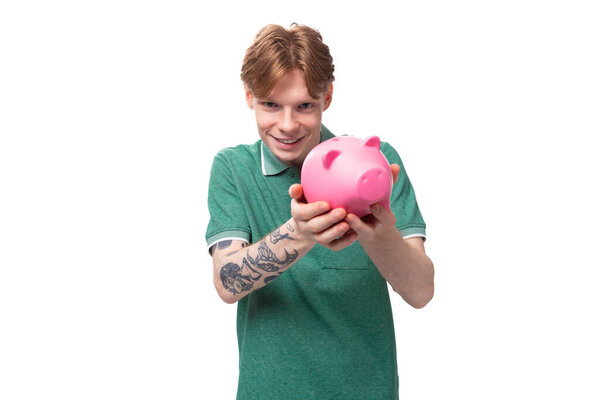 a young red-haired caucasian guy in a green t-shirt is about to empty his piggy bank.