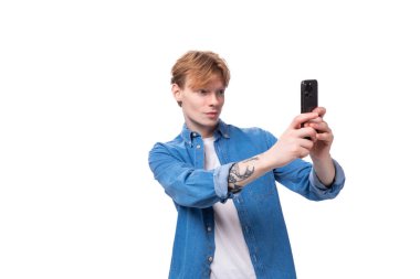 Kot mavi gömlekli, telefonda selfie çeken beyaz saçlı bir adamın portresi..