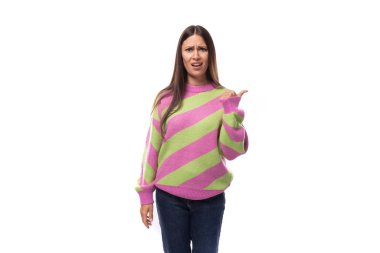 Şaşırtıcı genç Avrupalı esmer kadın çizgili pembe-yeşil kazak giymiş elleri boş uzayın arka planında hareketler yapıyor..