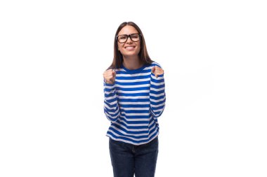 Mavi bluz ve beyaz arka planda fotokopi alanı olan kot pantolonlu iyimser, Avrupalı esmer bir kadının portresi..