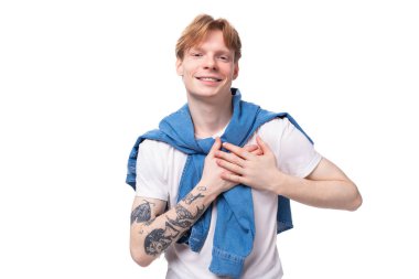 Genç, kısa saçlı, beyaz, altın sarısı saçlı, kollarında dövme olan erkek öğrenci beyaz bir tişört giyiyor..