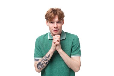 Yeşil tişört giymiş genç, kızıl saçlı adam arka plandaki fotokopi çekilen kameraya bakıyor..