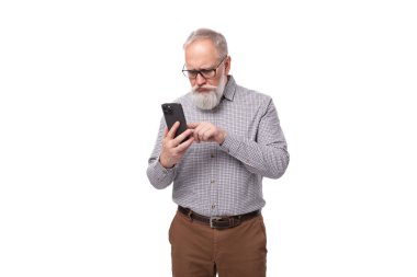 Gömleği ve pantolonu olan sakallı ve bıyıklı şık bir emekli adam telefonu anlıyor..