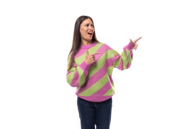 Sevimli, pozitif, neşeli, Avrupalı esmer kadın çizgili pembe yeşil kazak noktaları giymiş eli boş uzaya doğru..