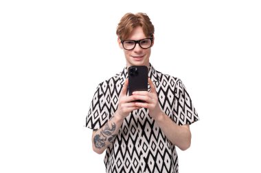 Gözlüklü, kızıl saçlı ve kollarında kısa kollu gömlek olan yakışıklı bir adam telefonda selfie çekiyor..