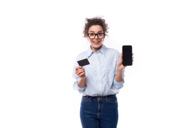 Açık mavi gömlekli genç, kıvırcık esmer sekreter bir kredi kartı ve ekranı öne bakan bir akıllı telefon modeli tutuyor. e-iş konsepti.