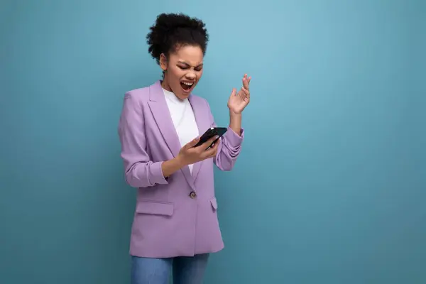 young pretty cute hispanic business woman with curly hair in a lilac jacket screaming while looking into a smartphone.