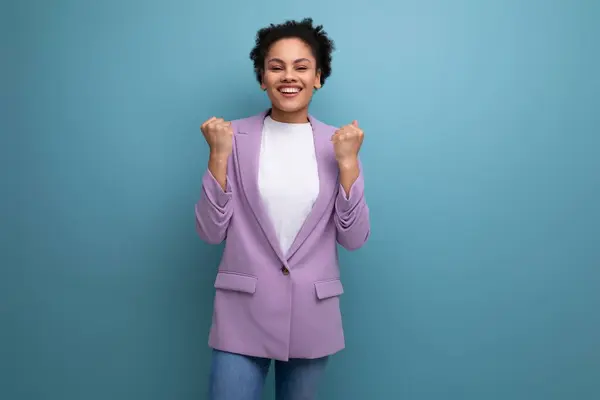 young successful latin woman with afro hair dressed in a lilac jacket on a studio background.