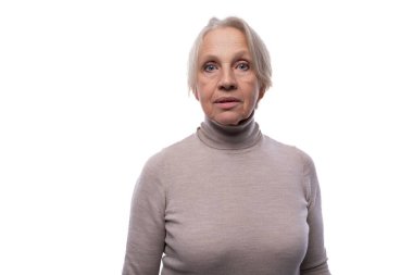 65 yaşında, kısa saçlı, emekli bir kadın kameraya dikkatle bakıyor..