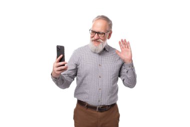 Gri saçlı, sakallı, bıyıklı ve gömlekli olgun bir adam telefonda selfie çekiyor..