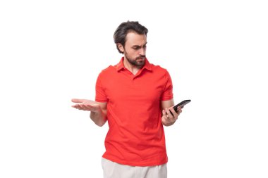 Siyah saçlı, sakallı, kırmızı tişörtlü genç yakışıklı adam akıllı telefon kullanarak ellerini kaldırıyor..
