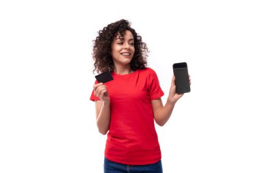 Kırmızı tişörtlü genç reklamcı kadın elinde akıllı telefon ve çevrimiçi çeviri için plastik kart tutuyor..