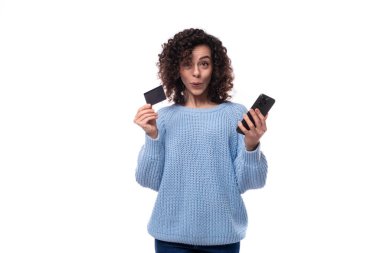 Kıvırcık saç stili olan genç ve güzel bir kadın elinde plastik kartlar ve akıllı bir telefon taşıyor..