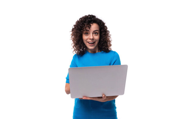 young curly woman with black hair is wearing a blue corporate t-shirt and holding a laptop.