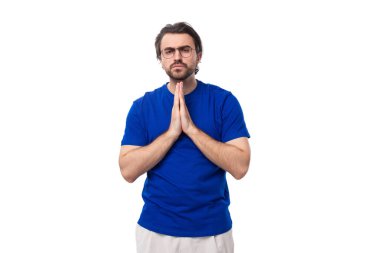 30 yaşında, siyah saçlı, mavi tişörtlü, sakallı, Avrupalı bir adam en iyisini umarak ellerini kavuşturdu..