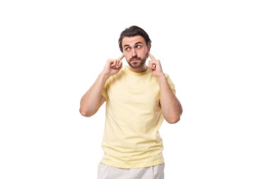 Sarı tişörtlü, sakallı, çekici, genç, esmer adam kulaklarını kapatmış..