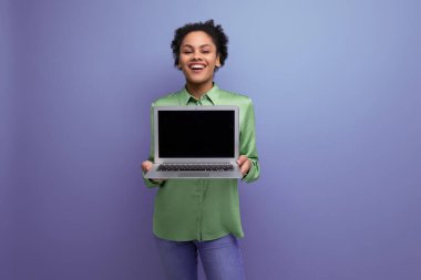 Genç, neşeli, pozitif esmer, yeşil şık bluz giymiş kadın elinde arka planda fotokopi alanı olan bir laptop tutuyor..
