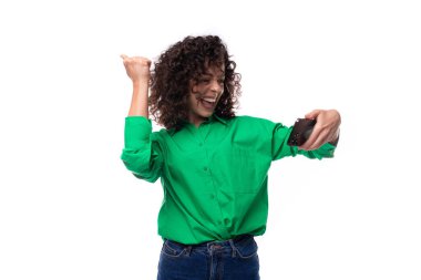 Yeşil bluz giymiş, siyah kıvırcık saçlı, gülümseyen genç kadın telefondaki videoya baktı..