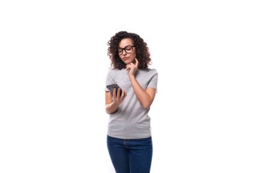 Kafkasyalı genç esmer kadın omuz hizasında kıvırcık saçlı akıllı bir telefona bakıyor..