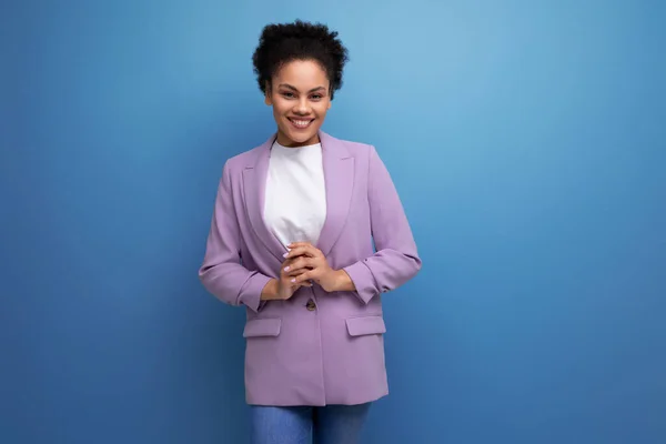 young successful latin woman with afro hair dressed in a lilac jacket on a studio background.
