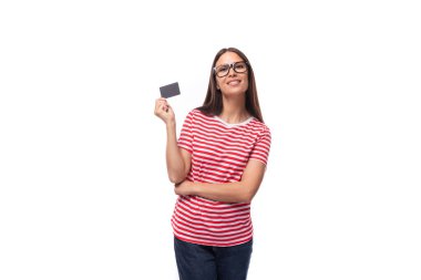 Düz saçlı, gözlüklü ve çizgili tişörtlü beyaz bir kadın elinde plastik bir kredi kartı modeli tutuyor. e-iş konsepti.