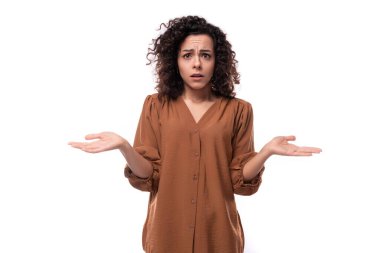 Kahverengi gömlekli esmer kadın beyaz arka planda düşünceli bir şekilde duruyor..