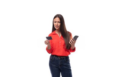 Kafkasyalı esmer, kırmızı bluz giymiş genç bir kadın plastik kart ve akıllı telefon kullanıyor. iş kavramı.