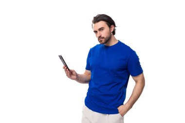 Mavi tişörtlü, sakallı genç esmer adam beyaz arka planda akıllı telefon kullanıyor..