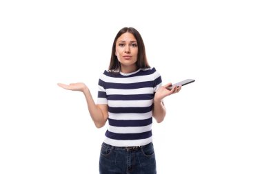 Siyah düz saçlı, çizgili siyah beyaz tişörtlü ve kot pantolonlu çekici genç Avrupalı kadın şüphe duyuyor ve kollarını farklı yönlere açıyor..