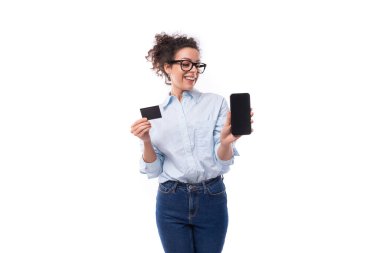 Açık mavi gömlekli, ince esmer, kıvırcık iş kadını akıllı telefon ekranı ve plastik kart gösteriyor..