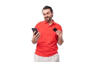 35 yaşında, bakımlı, kırmızı tişörtlü, sakallı, Avrupalı genç bir adam akıllı telefondan internet üzerinden ödeme yapıyor..