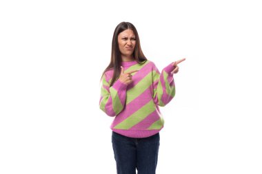 Sevimli, pozitif, neşeli, Avrupalı esmer kadın çizgili pembe yeşil kazak noktaları giymiş eli boş uzaya doğru..