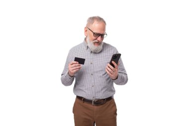 Beyaz sakallı ve bıyıklı büyükbaba, gömlek ve pantolon giymiş. Çevrimiçi tercümeler, kart ve akıllı telefon kullanıyor..