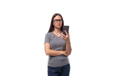 Gri tişört giymiş genç, tatlı, esmer Avrupalı kadın beyaz arka planda bir cep telefonu kullanıyor..