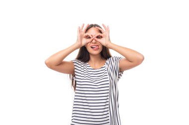 Genç, düz saçlı, gözlüklü esmer kadın çizgili tişört giyiyor ve kot pantolon, beyaz arka planda, fotokopi alanı olan bir suratını buruşturuyor..