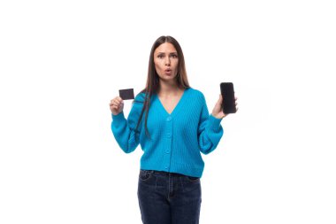 Siyah saçlı, mavi hırka giymiş çekici beyaz bir kadın kredi kartı ve ekranı öne bakan bir akıllı telefon gösteriyor. e-iş konsepti.