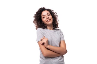 Beyaz arka planda gri tişörtlü, kıvırcık saçlı, hoş, genç, Avrupalı esmer bir kadının portresi..