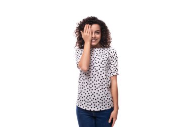 Kıvırcık saçlı, bluz giymiş, puantiyeli genç bir kadın gülümsüyor ve mutlu oluyor..