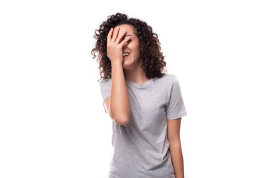 Gri tişört giymiş, siyah kıvırcık saçlı güzel beyaz kadın yüzünü kapatmaktan utanıyor..