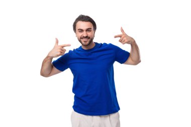 Mavi tişörtlü, sakallı, genç, yakışıklı, esmer bir adam. Aktif olarak elleri fotokopi çekilen beyaz bir arka planda hareket ediyor..