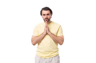 Yazlık tişört giymiş, sakallı, vahşi, beyaz, yakışıklı bir adam ellerini kavuşturdu..