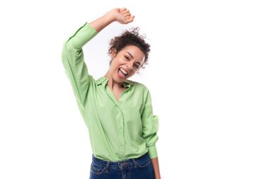Genç, pozitif, neşeli, Avrupalı, kıvırcık saçlı, at kuyruklu, kıvırcık saçlı kadın yeşil bir gömlek giyiyor ve beyaz bir arka planda fotokopi alanı ile gülümsüyor..