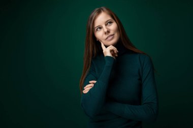 30 yaşında, kahverengi saçlı, Avrupalı bir kadın. Siyah arka planda yeşil balıkçı yaka bir kazak giyiyor..