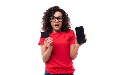 Siyah kıvırcık saçlı, kırmızı tişörtlü, elinde akıllı telefon ve kart modeliyle neşeli, şen şakrak beyaz kadın..