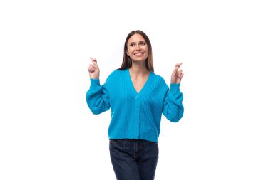 young pretty smiling brunette woman in a blue cardigan crossed her fingers in anticipation of a miracle.