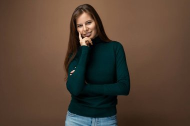 Stüdyo arka planında uzun kahverengi saçlı, kendinden emin, beyaz bir kadın..