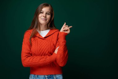 Kırmızı kazaklı, kendine güveni olan, koyu yeşil arka planda kendine güvenen genç bir kadın..