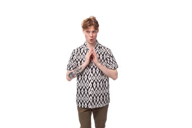 Genç, bakımlı, kızıl saçlı adam kısa kollu ve desenli bir gömlek giyiyor..